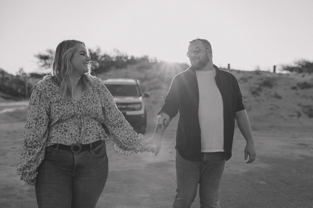 Couple smiles to each other while holding hands.