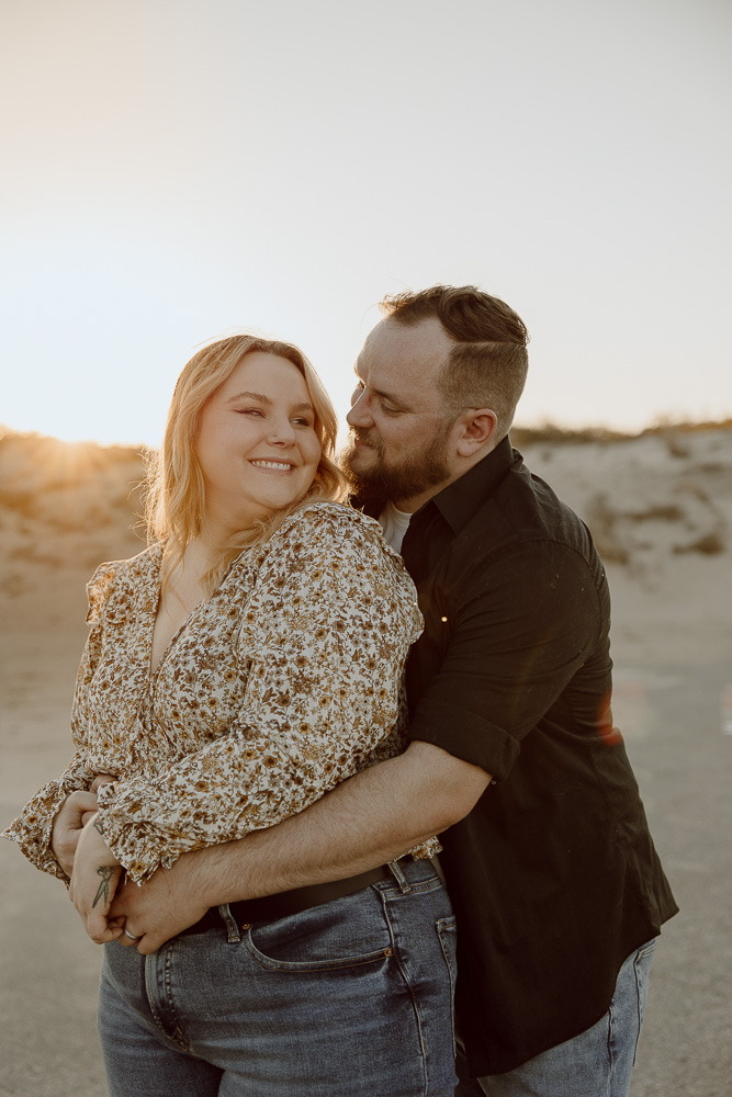 couple stands close and smiles at each other.