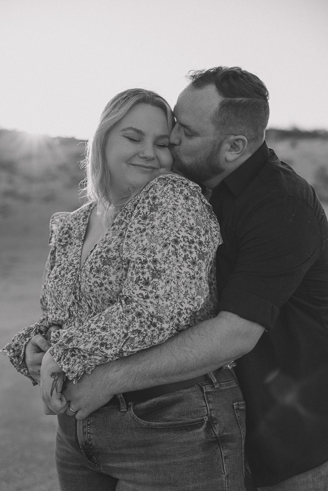 man hugs his partner from behind and kisses her forehead.