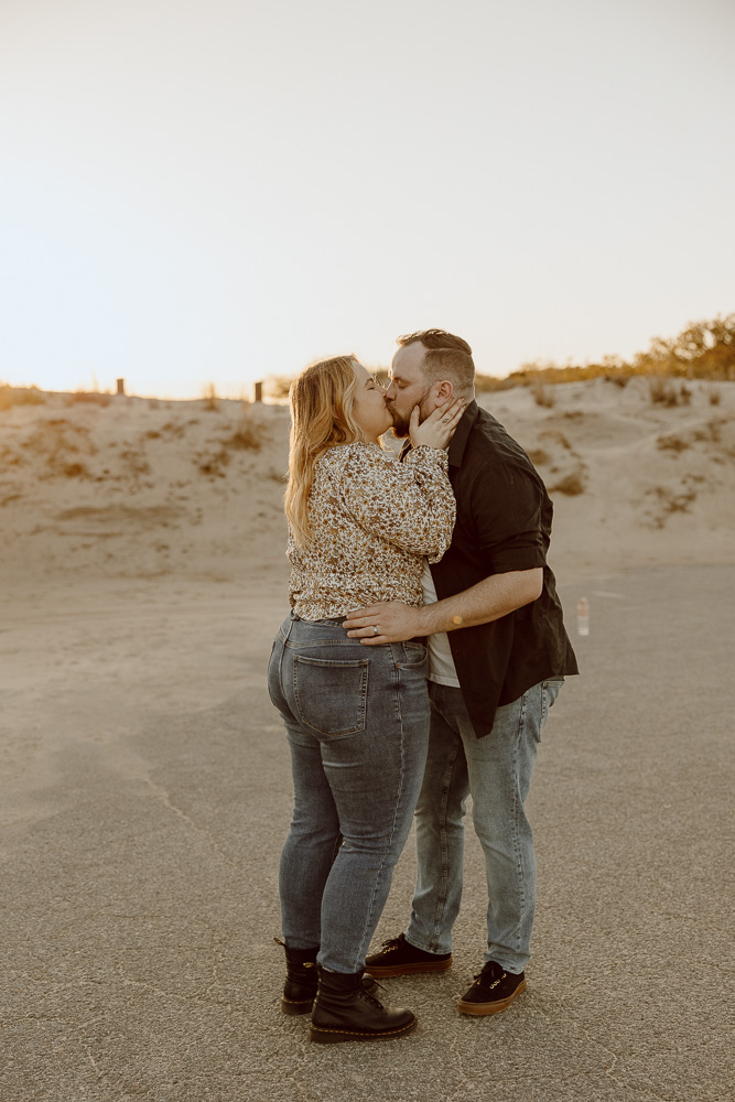 couple shares a kiss in beach parking lot during sunset.