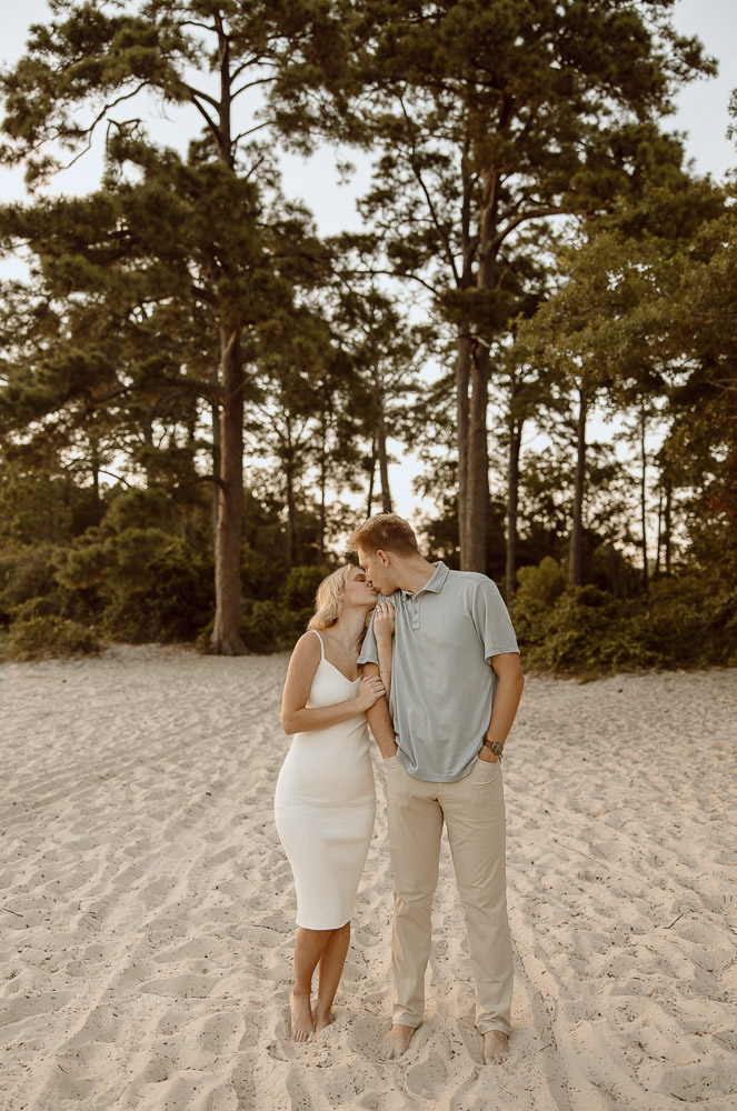 Couple stands side by side with their arms wrapped around each other and sharing a kiss.