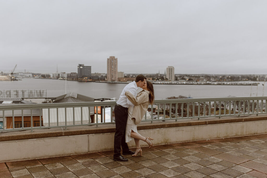 Couple shares a dip kiss as they stand on rooftop overlooking the Norfolk Virginia skyline.