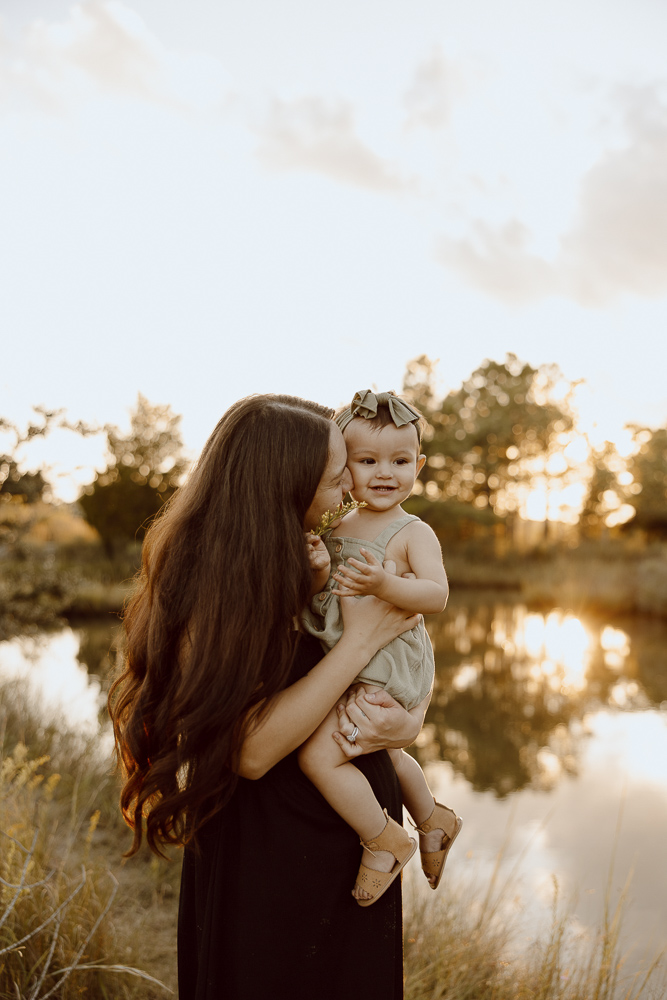 Mom and daughter smiling and cuddling during sunset.