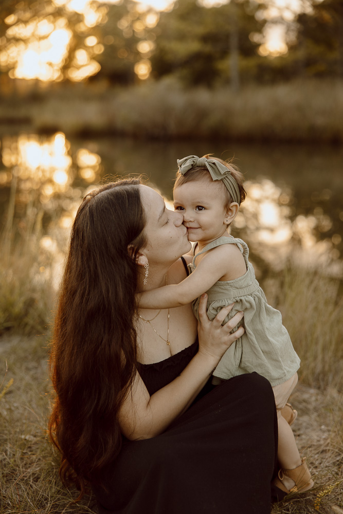 couple bends down to toodler daughter and holds her tight while kissing her cheek.