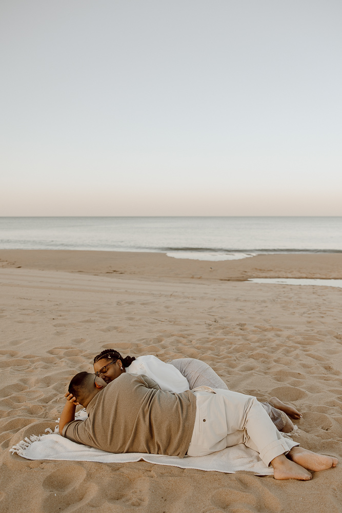 couple lays on a blanket facing each other while on an empty beach in Virginia Beach.