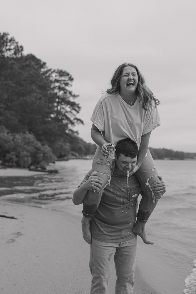 Girl laughs as she pours beer into her boyfriends mouth as she sits on his shoulders.