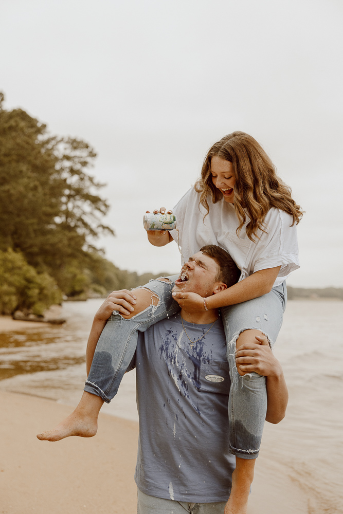 Girl pours beer into her boyfriends mouth as she sits on his shoulders.