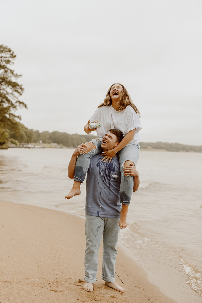 Girl laughs as she pours beer into her boyfriends mouth as she sits on his shoulders.