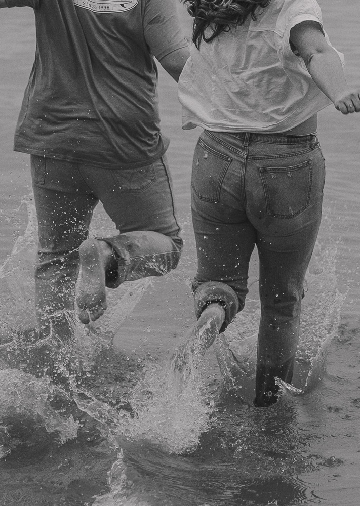 a couple holds hands and runs into the water together.