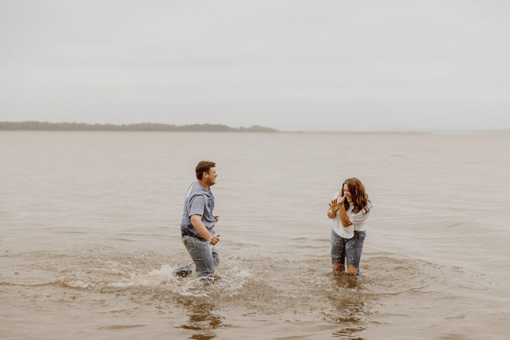 Couple stands in the middle of a lake splashing water on each other