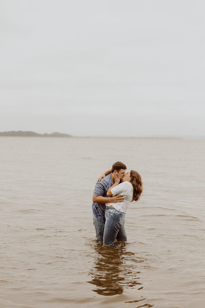 after running into the water fully clothed, a couple stands together and shares a kiss.