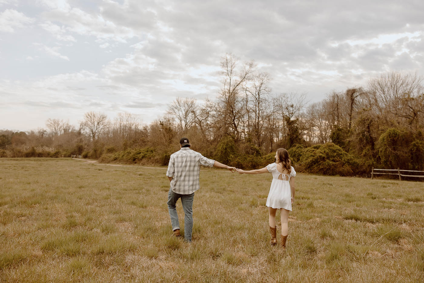 Couple holding hands walking through a field.