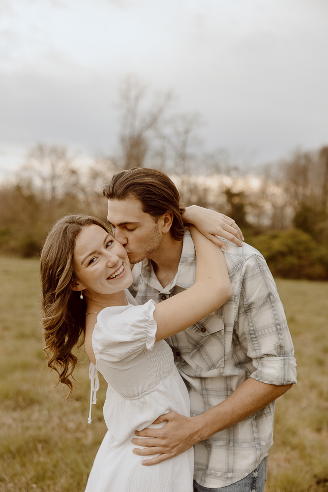 Man kisses his fiancée on the cheek during engagement photos.