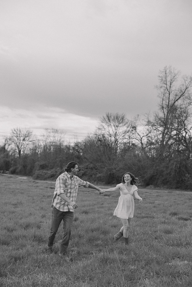 Couple running through open field while holding hands.