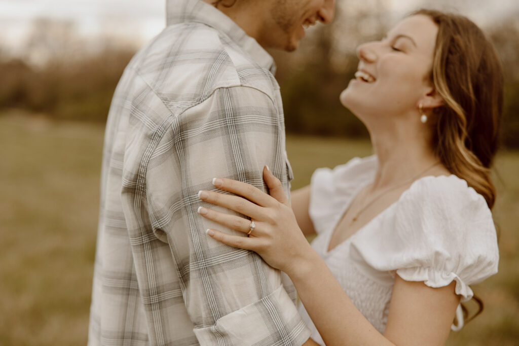 couple smiles at each other while showing engagement ring.