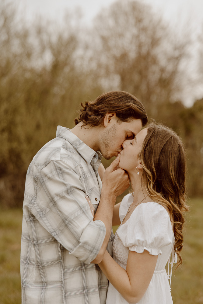 Couple shares a kiss while he puts a hand on her chin.