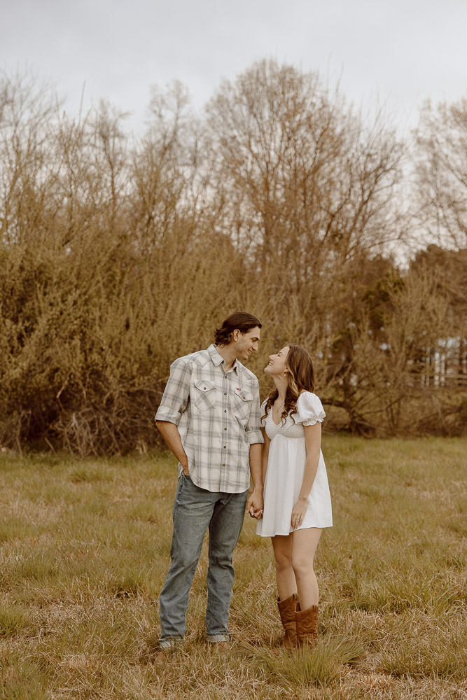 Couple holding hands and smiling at each other in a field.