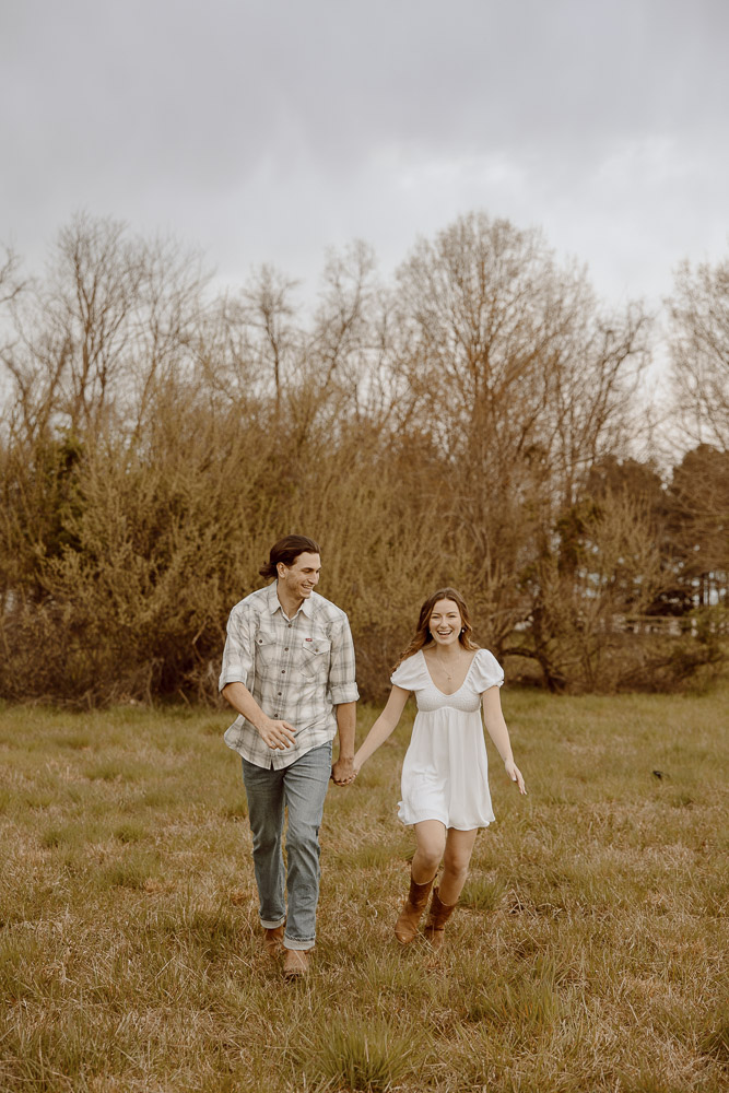 Couple laughing and running in a field.