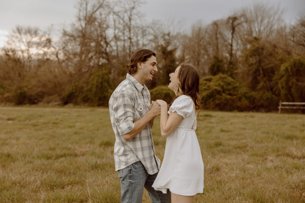 Couple smiling and laughing at each other while dancing in a field.