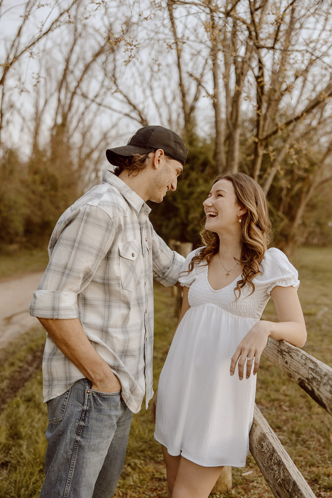 Couple smiling to each other while leaning onto fence posting.