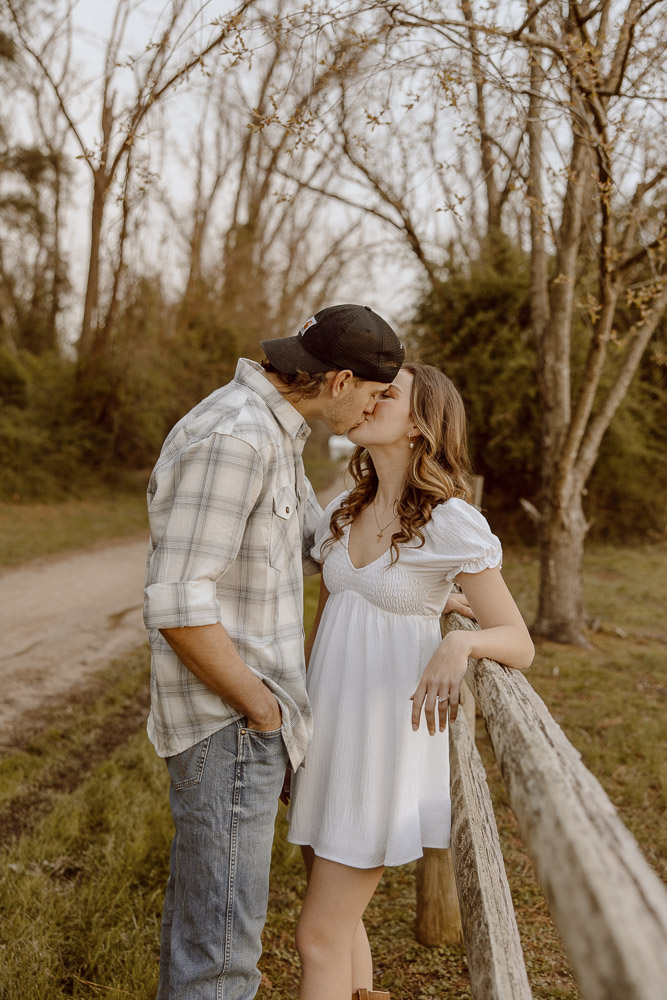 Couple shares a kiss while leaning on a fence.