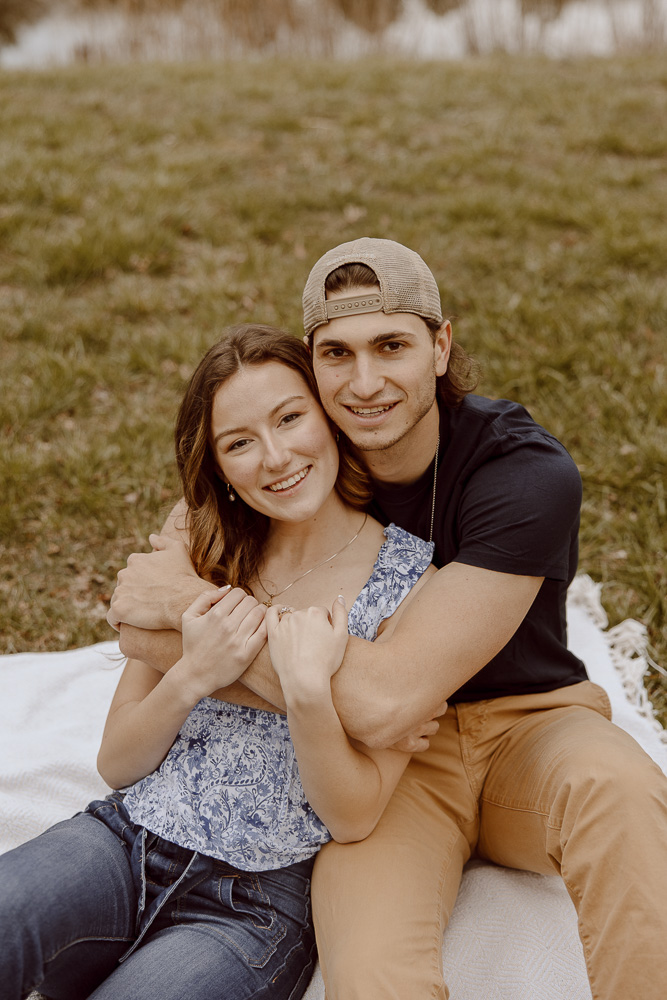 Couple smiling towards camera while sitting on a blanket.