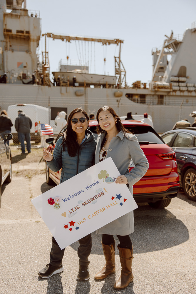 Military spouses standing in front of Navy ship at homecoming.