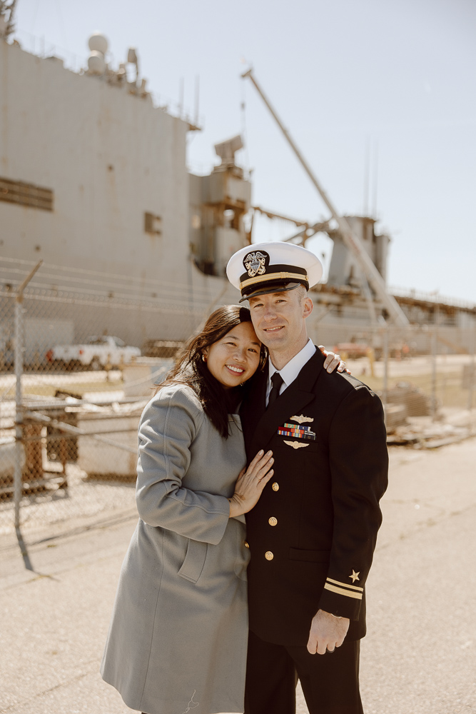 A navy sailor and his wife smiling and hugging while standing next to USS Carter Hall.