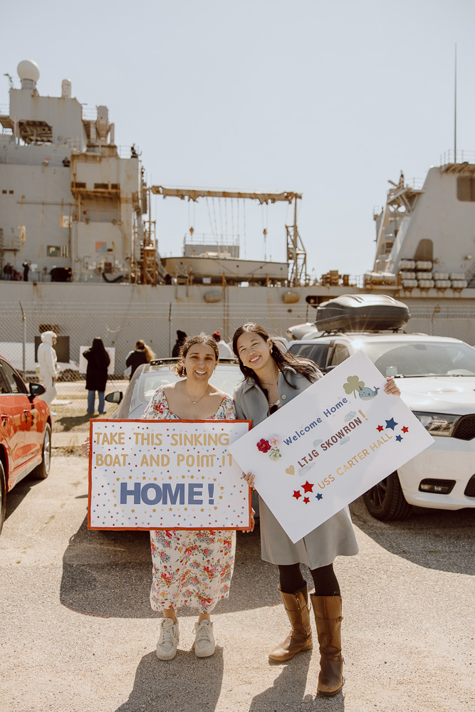 Military spouses standing in front of Navy ship at homecoming.