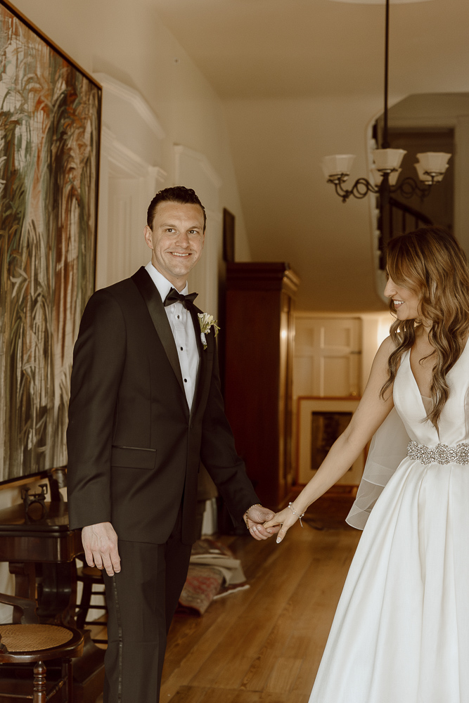 Bride and groom hold hands and smile at each other.