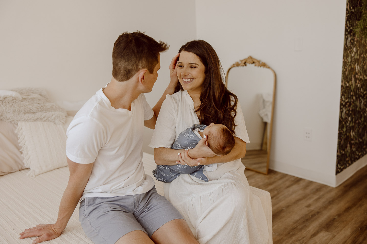 A new dad runs his fingers through his wife's hair as she smiles at him and holds their newborn baby boy.