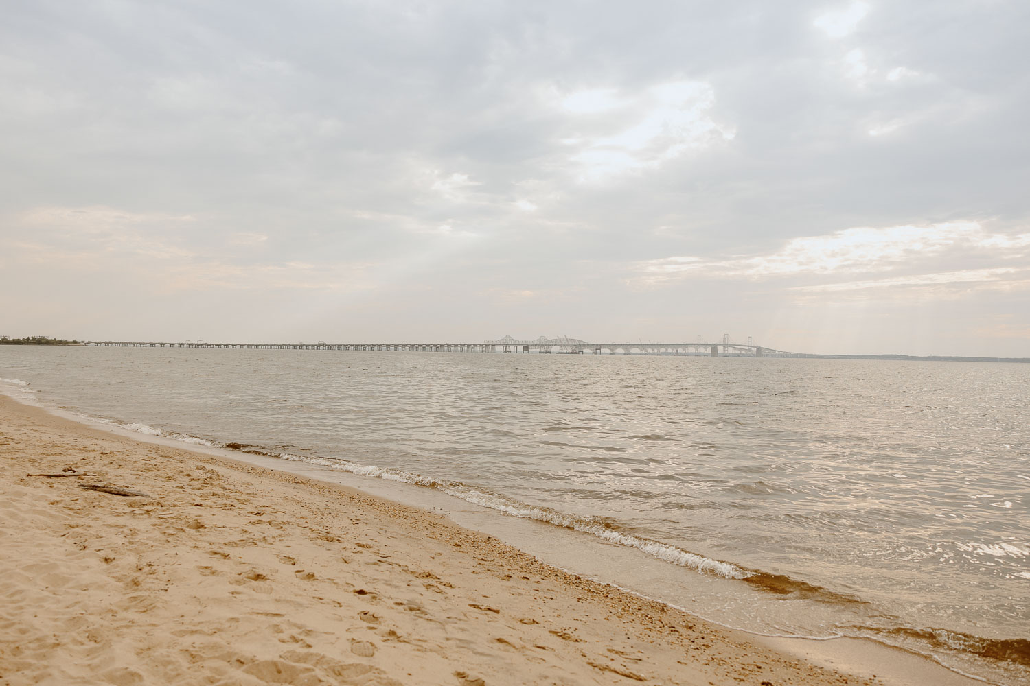 A beach at sunset with a few of the Chesapeake Bay Bridge.