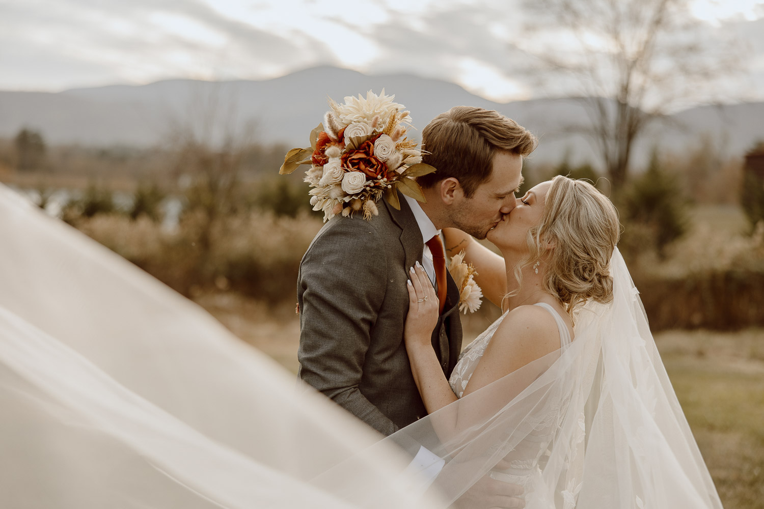 Bride and Groom share a kiss while the veil swoops through the camera lens.