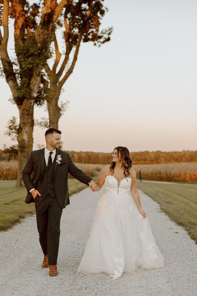 Bride and groom walk while holding hands and smiling.