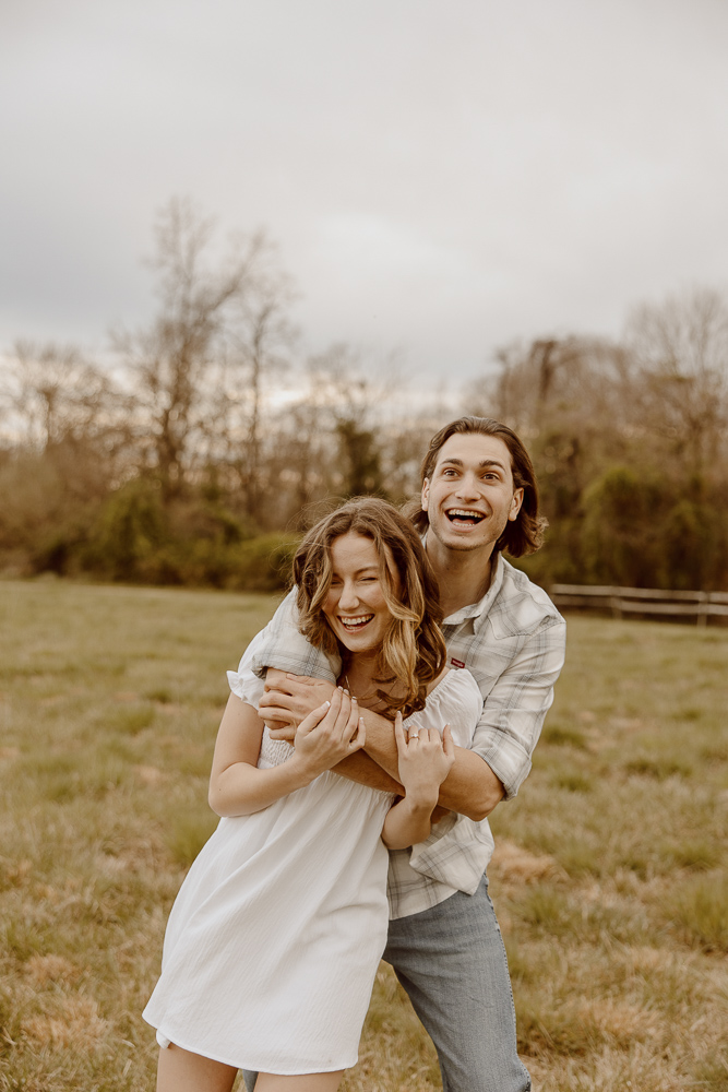 A couple laughs while dancing around during their engagement session in a field on Kent Island.