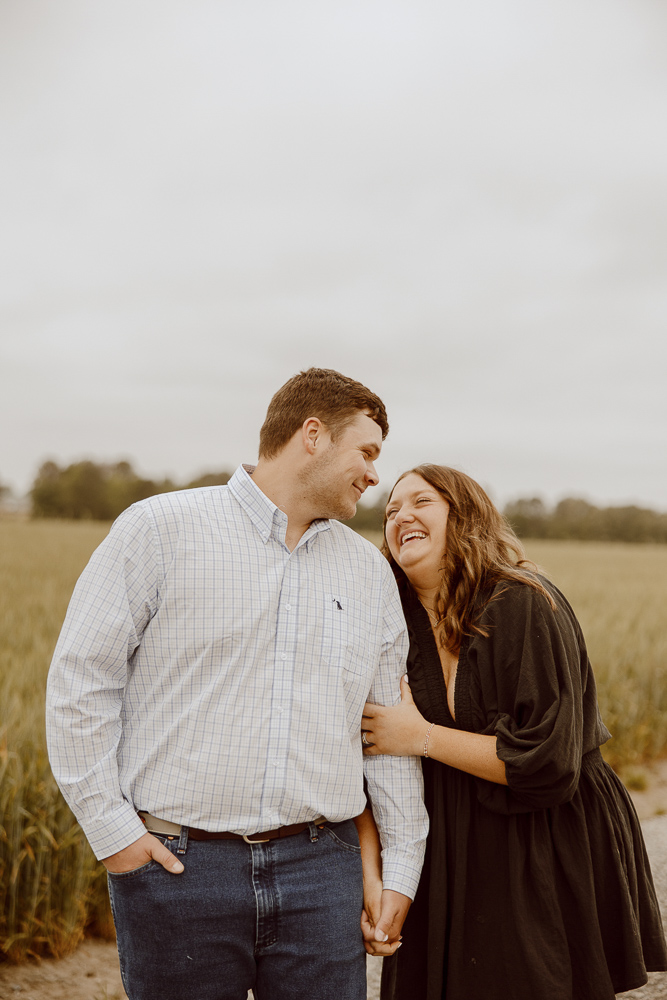 A couple stands together and holds hands while laughing.