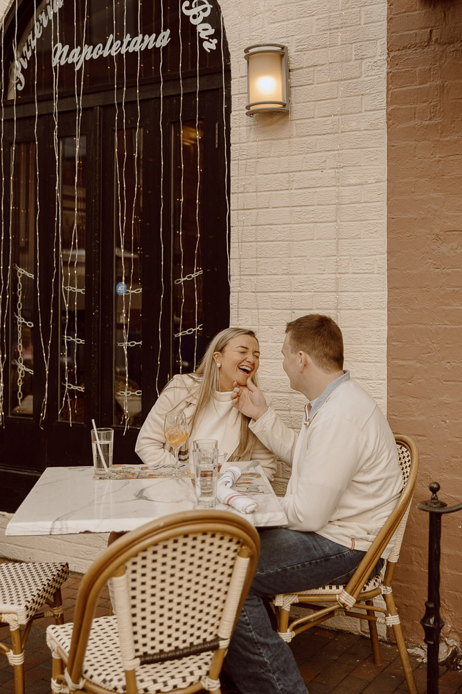 Couple laughs together while sitting at an outdoor table at downtown Italian restaurant.