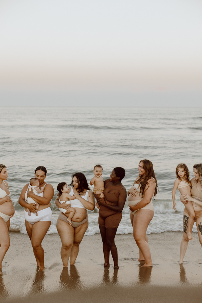 A group of mothers stand together on the beach while wearing skin-toned undergarments.